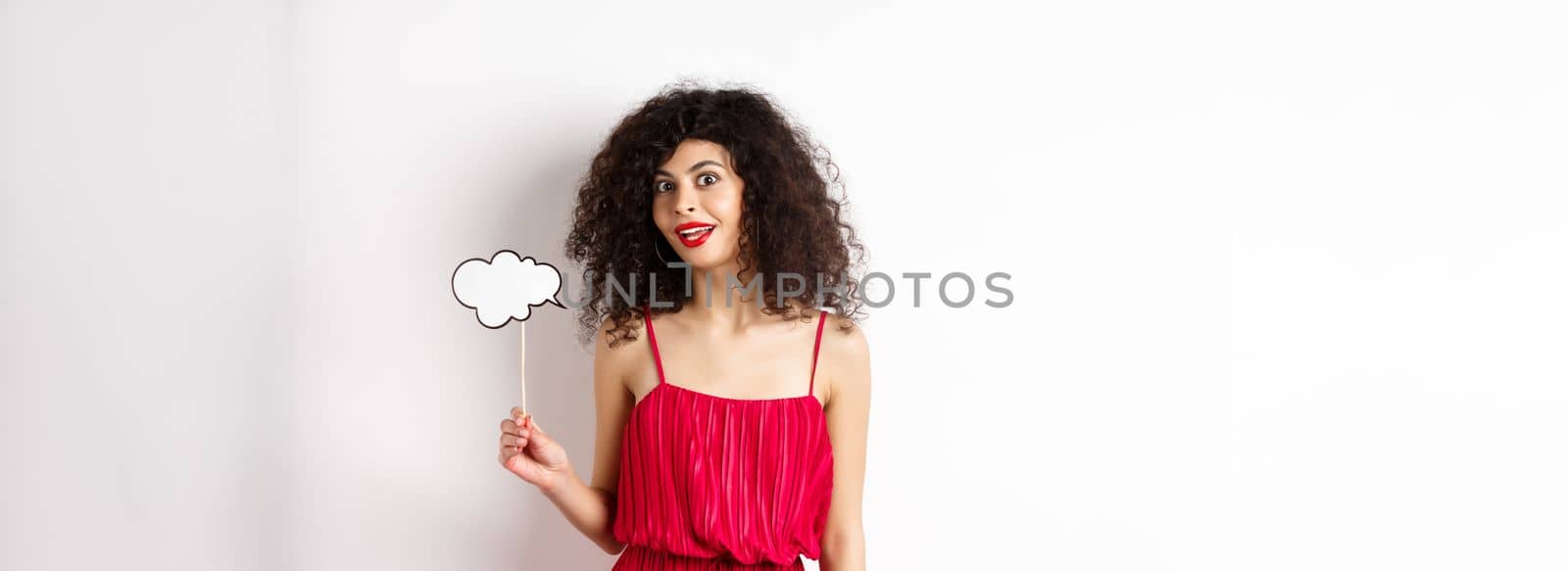 Beautiful woman with curly hair, wearing red dress, holding comment cloud, say something, standing on white background.