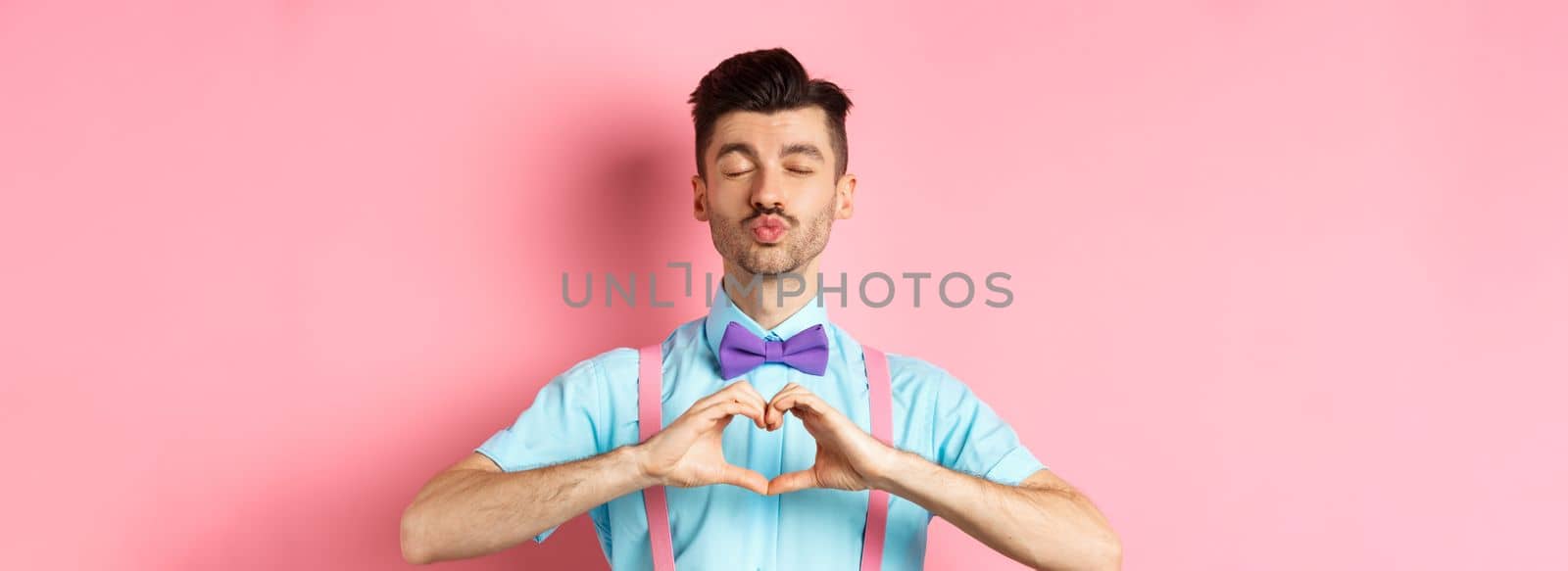 Happy Valentines day. Romantic boyfriend close eyes for kiss and showing heart, having date with lover, standing over pink background by Benzoix