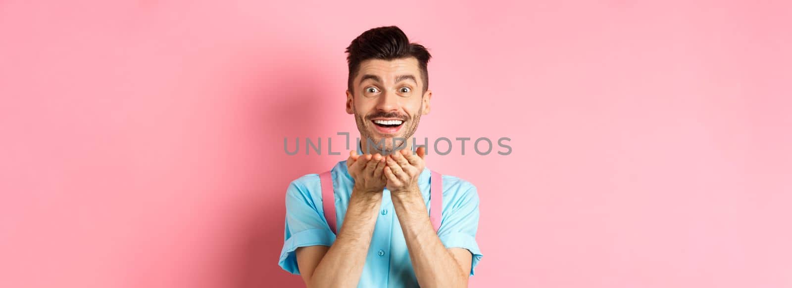 Man in love blowing kiss at camera and smiling passionate, looking at lover happy, enjoying Valentines day, standing over pink background.