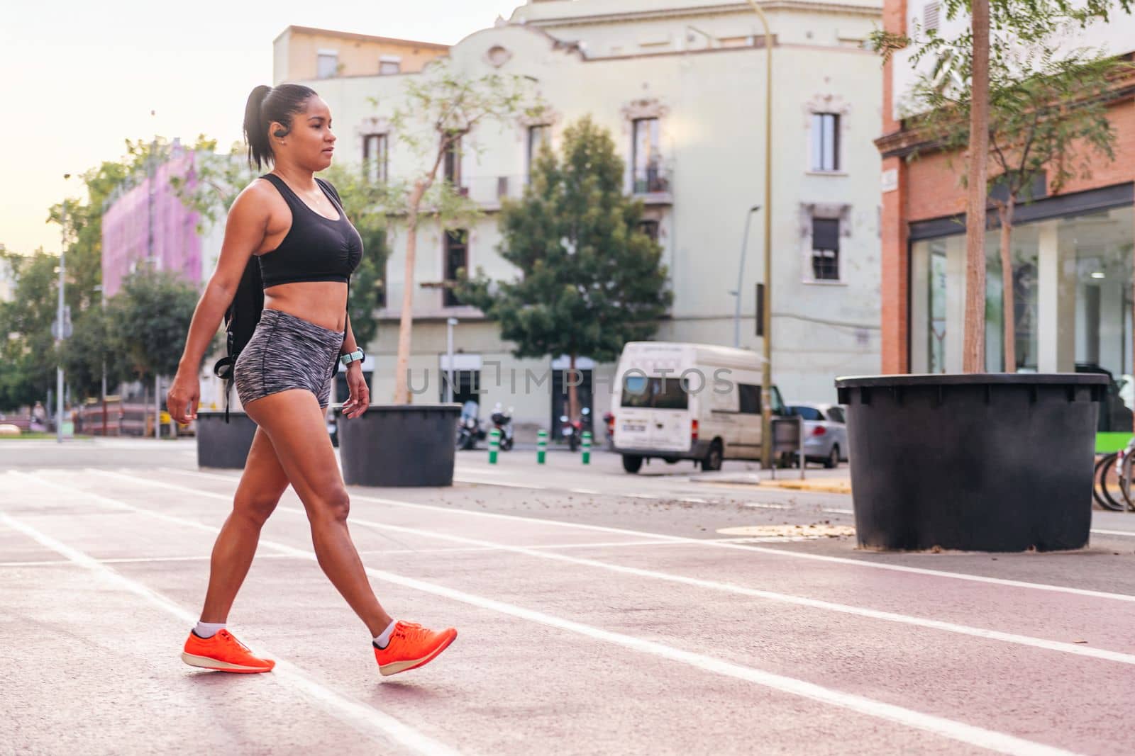 latina sportswoman walking with a backpack on a city athletics track, urban sports and healthy lifestyle concept, copy space for text