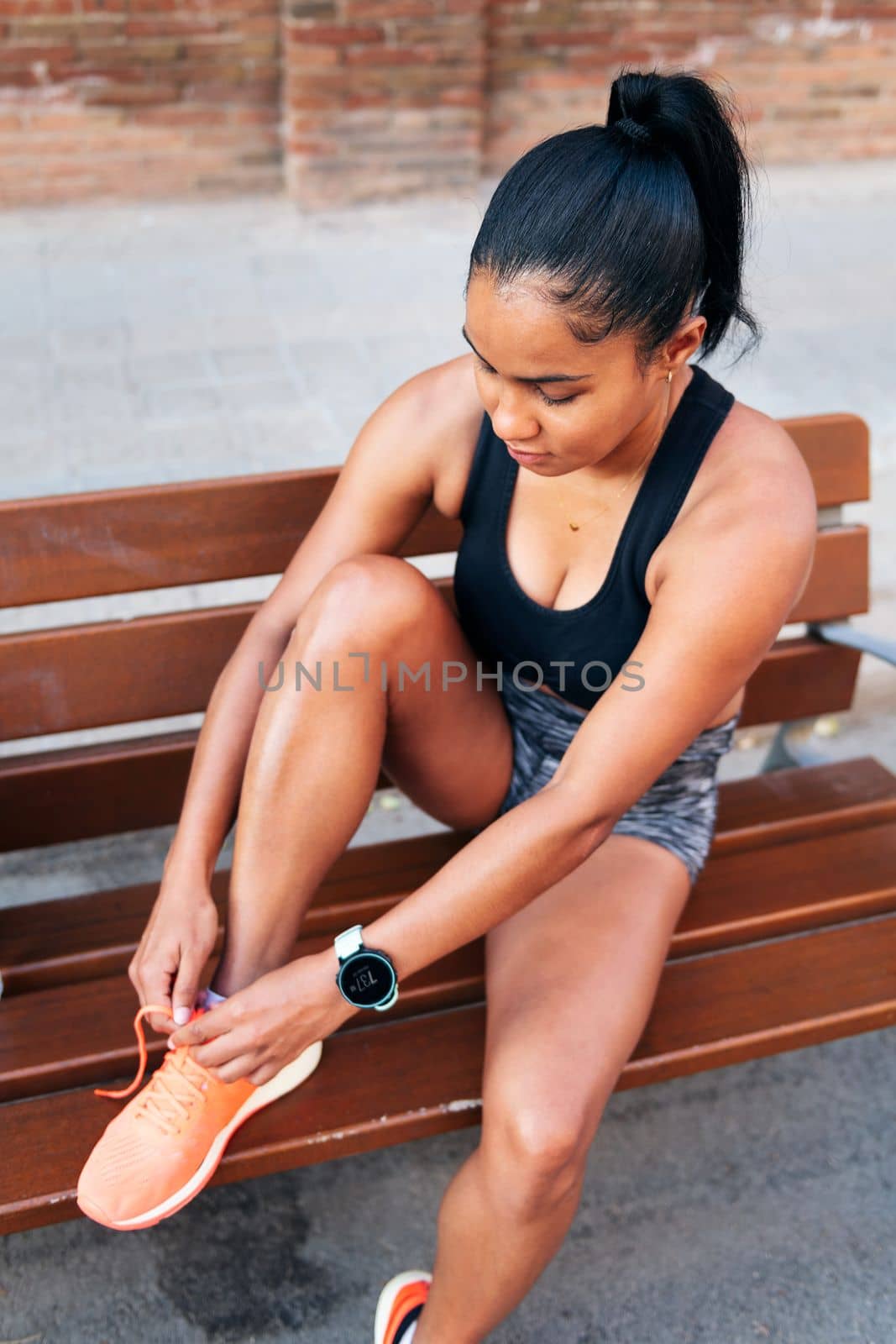 latin sportswoman lacing up her running shoes before her workout, urban sport and healthy lifestyle concept