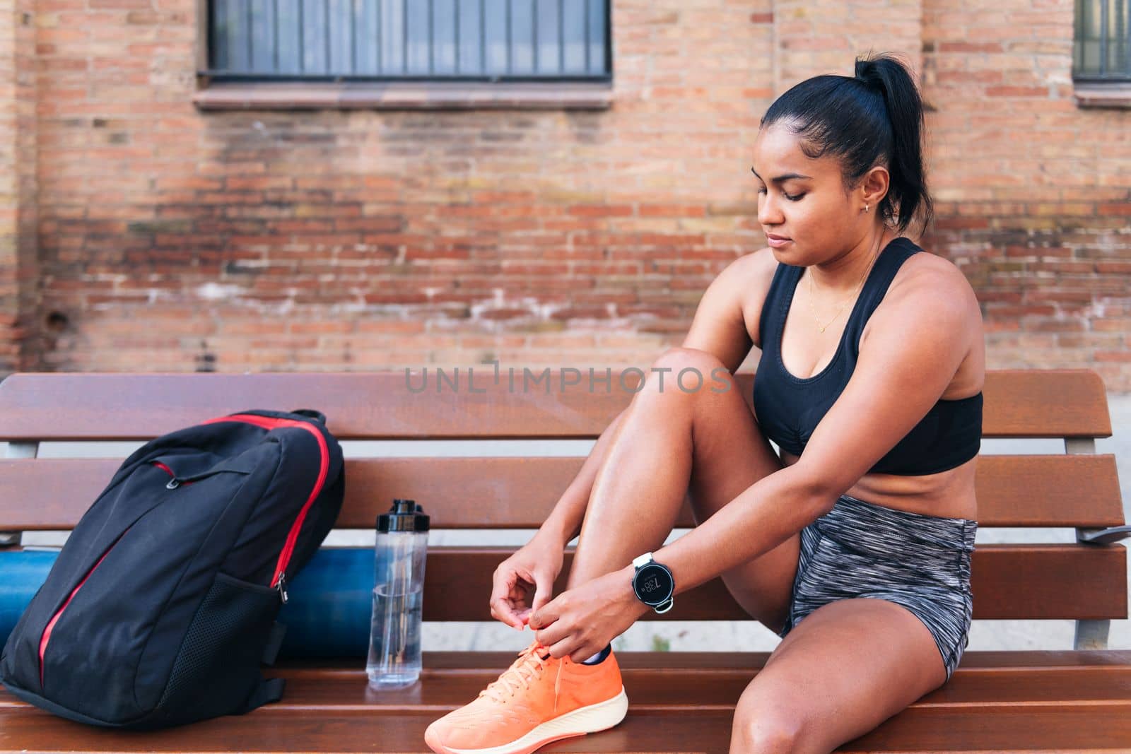 latin sportswoman lacing up her running shoes before her workout, urban sport and healthy lifestyle concept, copy space for text