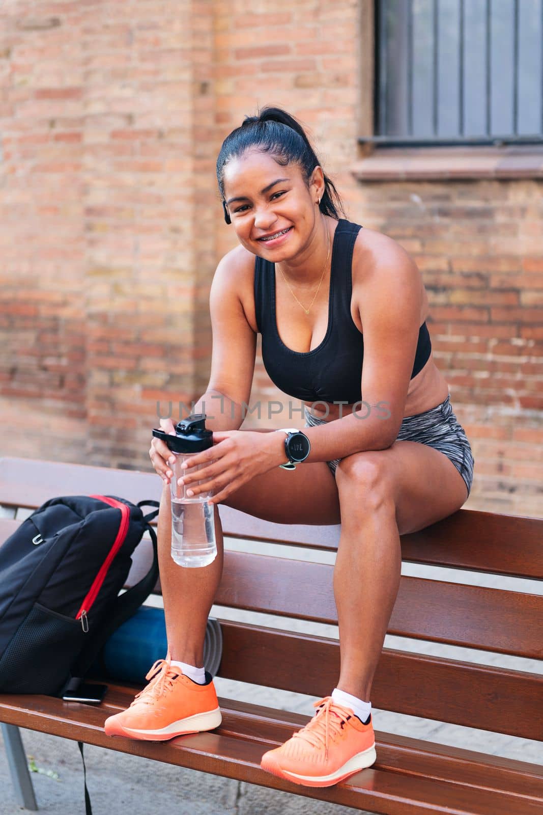 latin sportswoman with a bottle of water smiling looking at camera, urban sports and healthy lifestyle concept, copy space for text