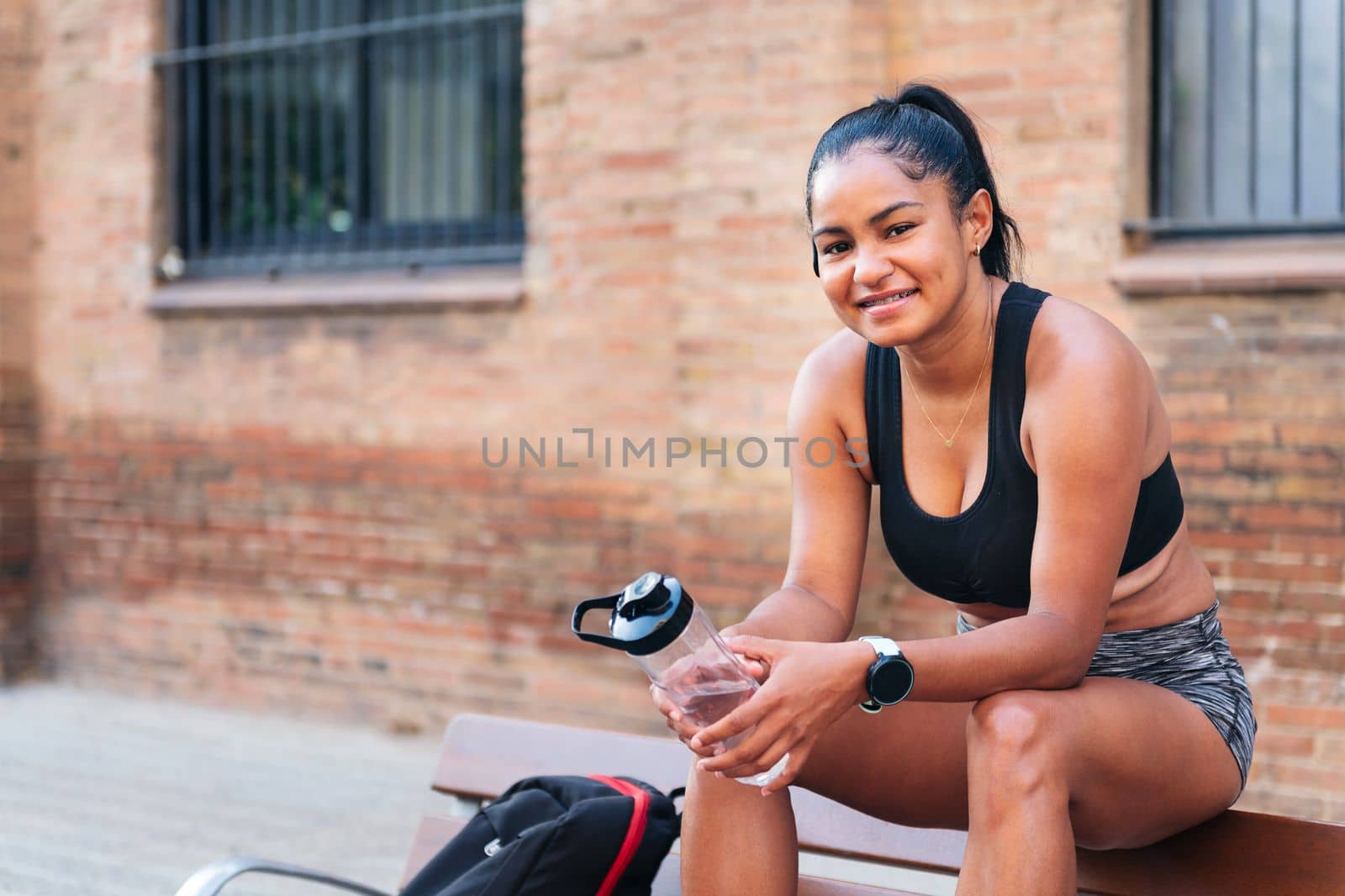 latin sportswoman with a bottle of water smiling looking at camera, urban sports and healthy lifestyle concept, copy space for text