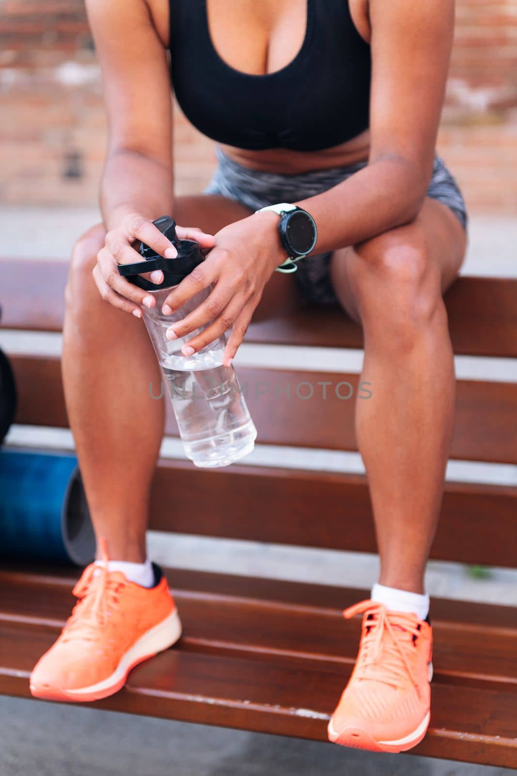 detail of the hands of an unrecognizable sportswoman holding a bottle of water while resting on a bench during a break in her training, urban sport and healthy lifestyle concept