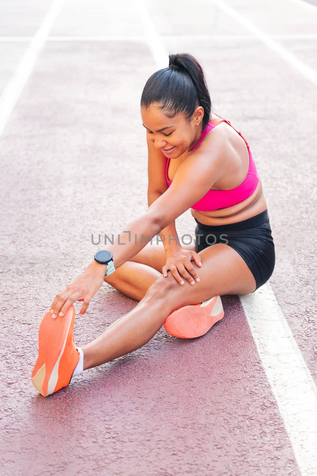 female athlete stretching legs sitting on the athletics track during her training, concept of urban sport and healthy lifestyle, copy space for text