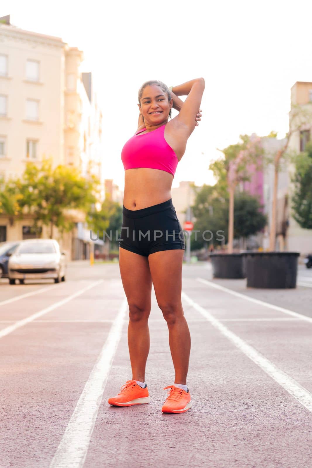 smiling sportswoman stretching arms on the athletics track of the city during her workout, concept of urban sport and healthy lifestyle, copy space for text