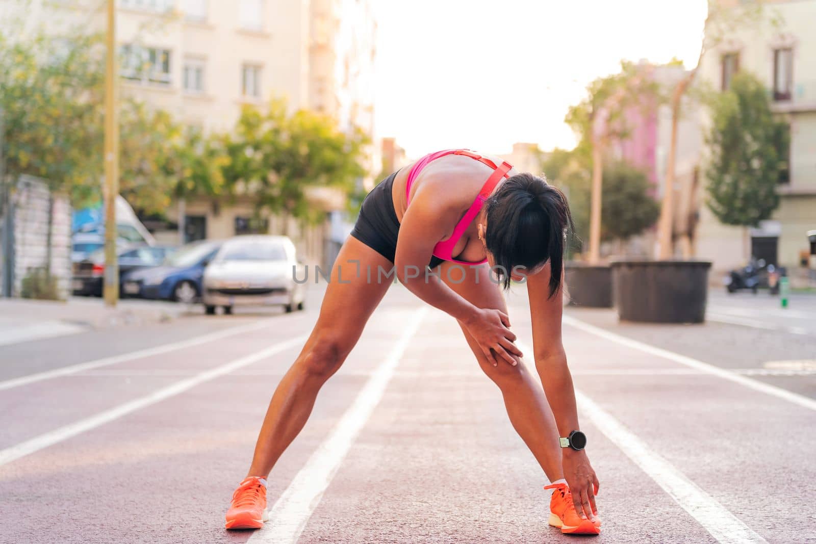 unrecognizable sportswoman stretching legs on the athletics track of the city during her training, concept of urban sport and healthy lifestyle, copy space for text