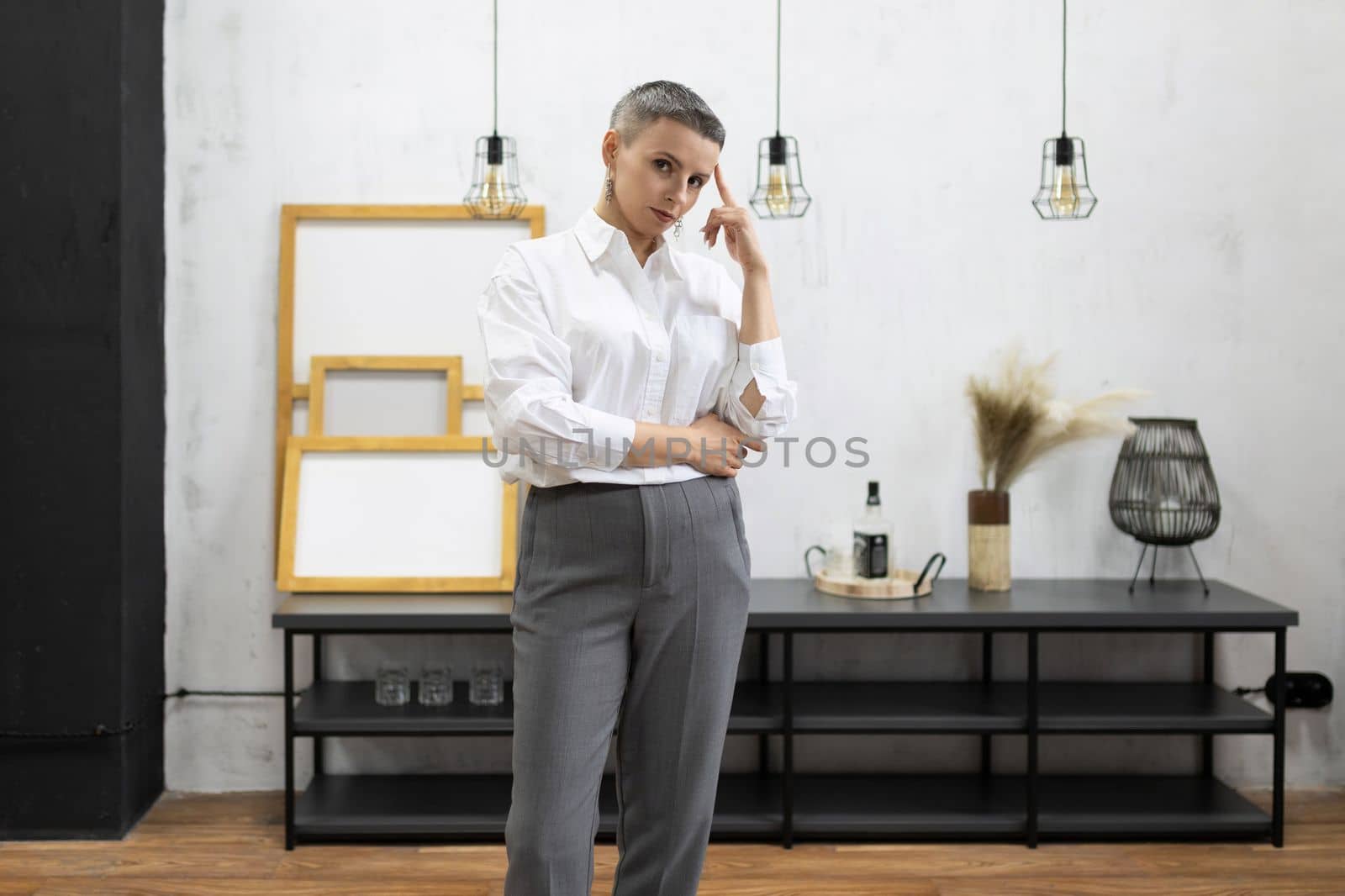 strong mature woman designer in white shirt and gray pants inside by TRMK