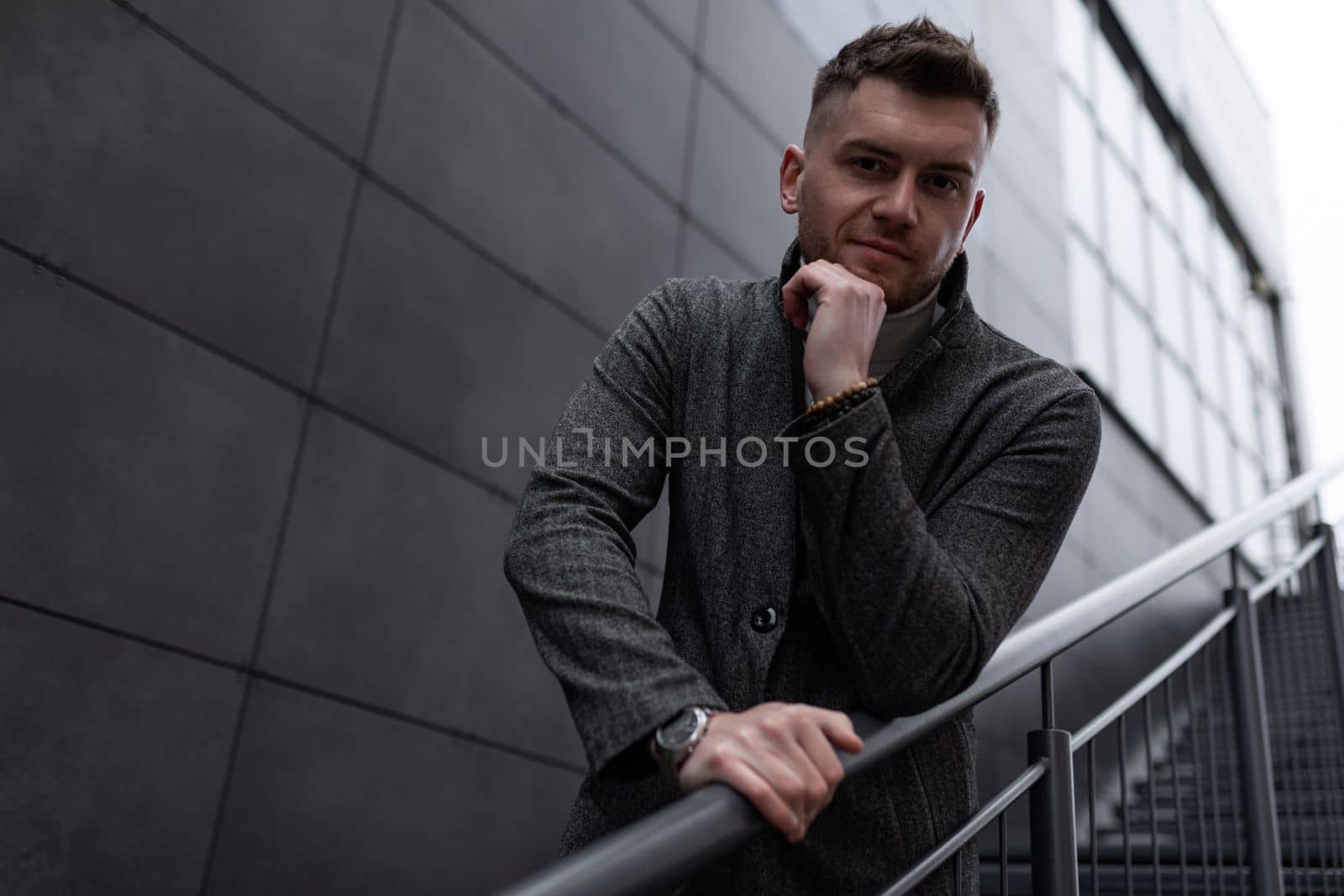stylish business brutal man stands on the steps on the stairs by TRMK