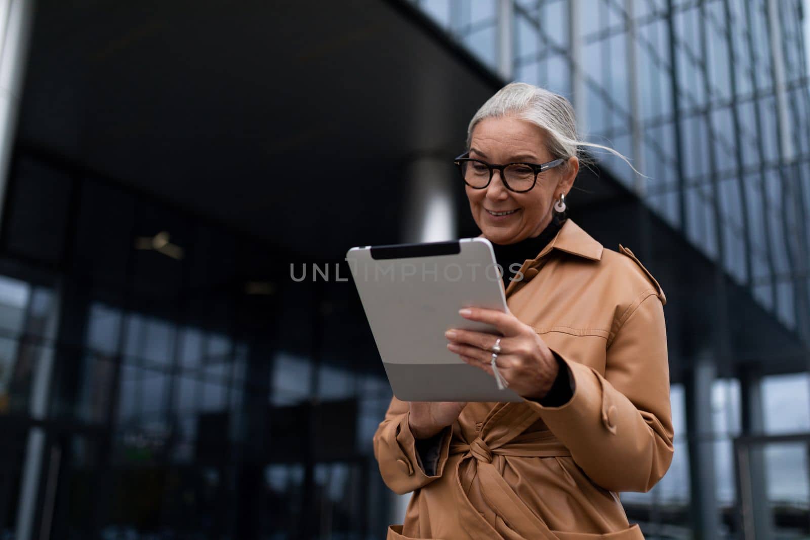mature elderly businesswoman with a tablet on the background of an office building by TRMK
