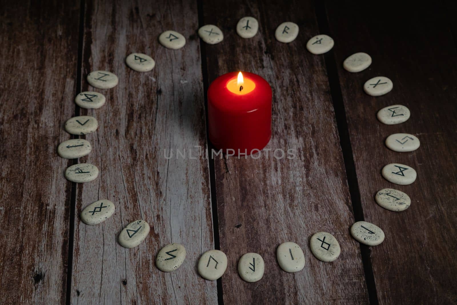 rune stones with black symbols for fortune telling with candles on a wooden table