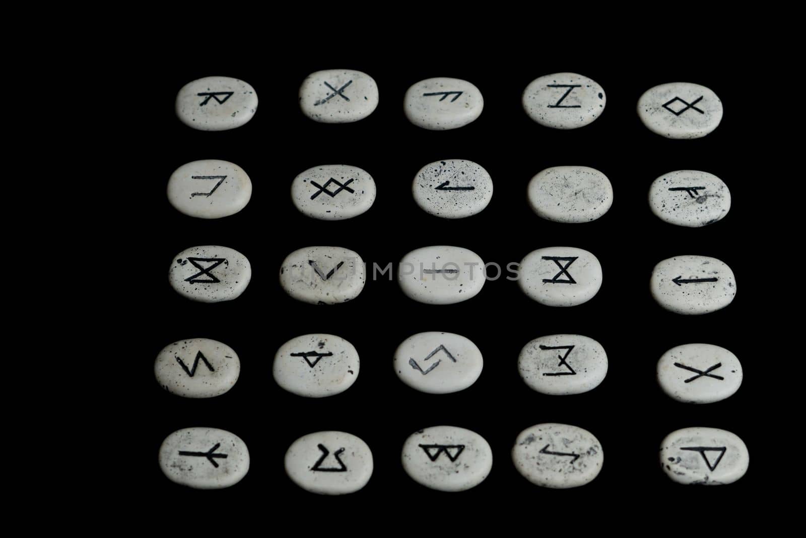 rune stones with black symbols for fortune telling with candles on a wooden table