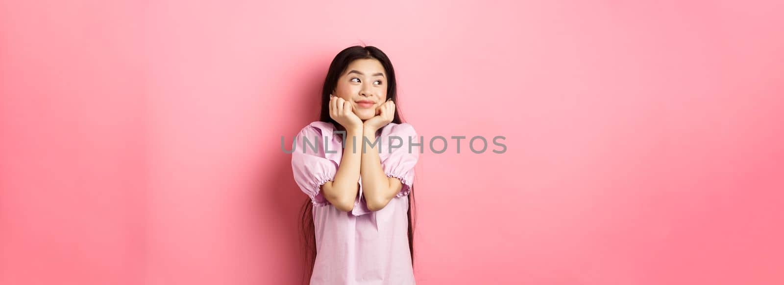 Dreamy romantic girl looking aside at logo and smiling, thinking of something beautiful, standing on pink background by Benzoix