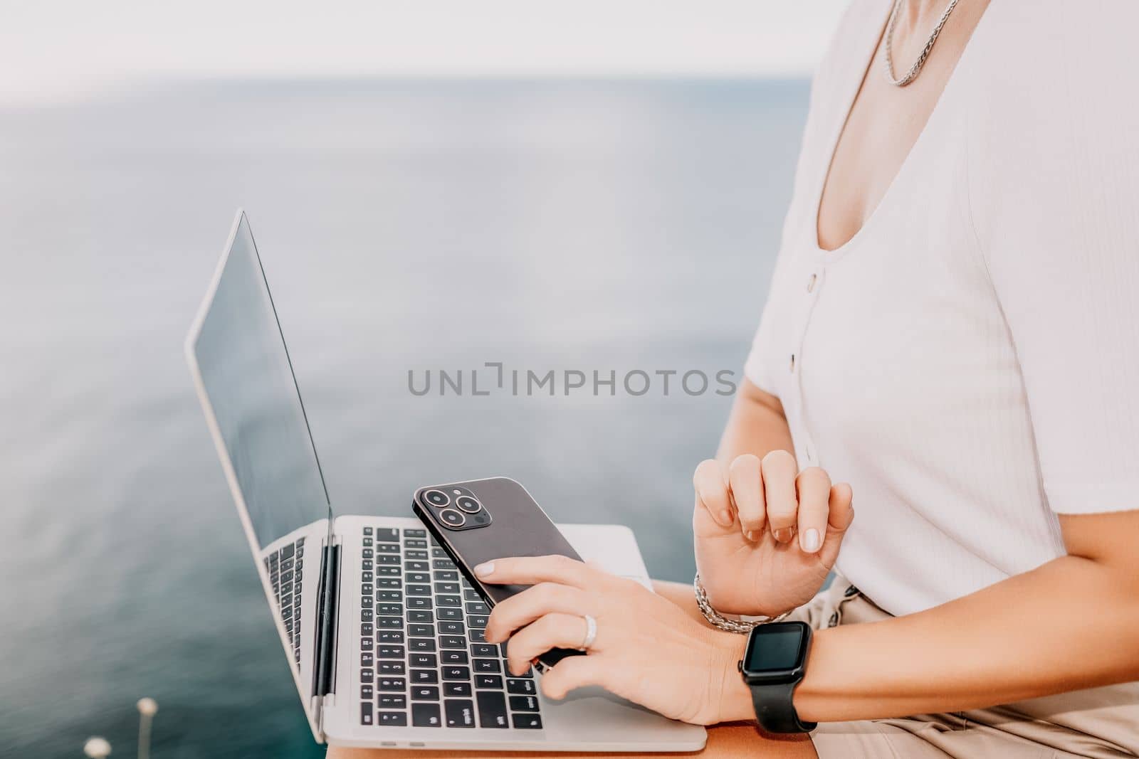 Digital nomad, Business woman working on laptop by the sea. Pretty lady typing on computer by the sea at sunset, makes a business transaction online from a distance. Freelance, remote work on vacation by panophotograph