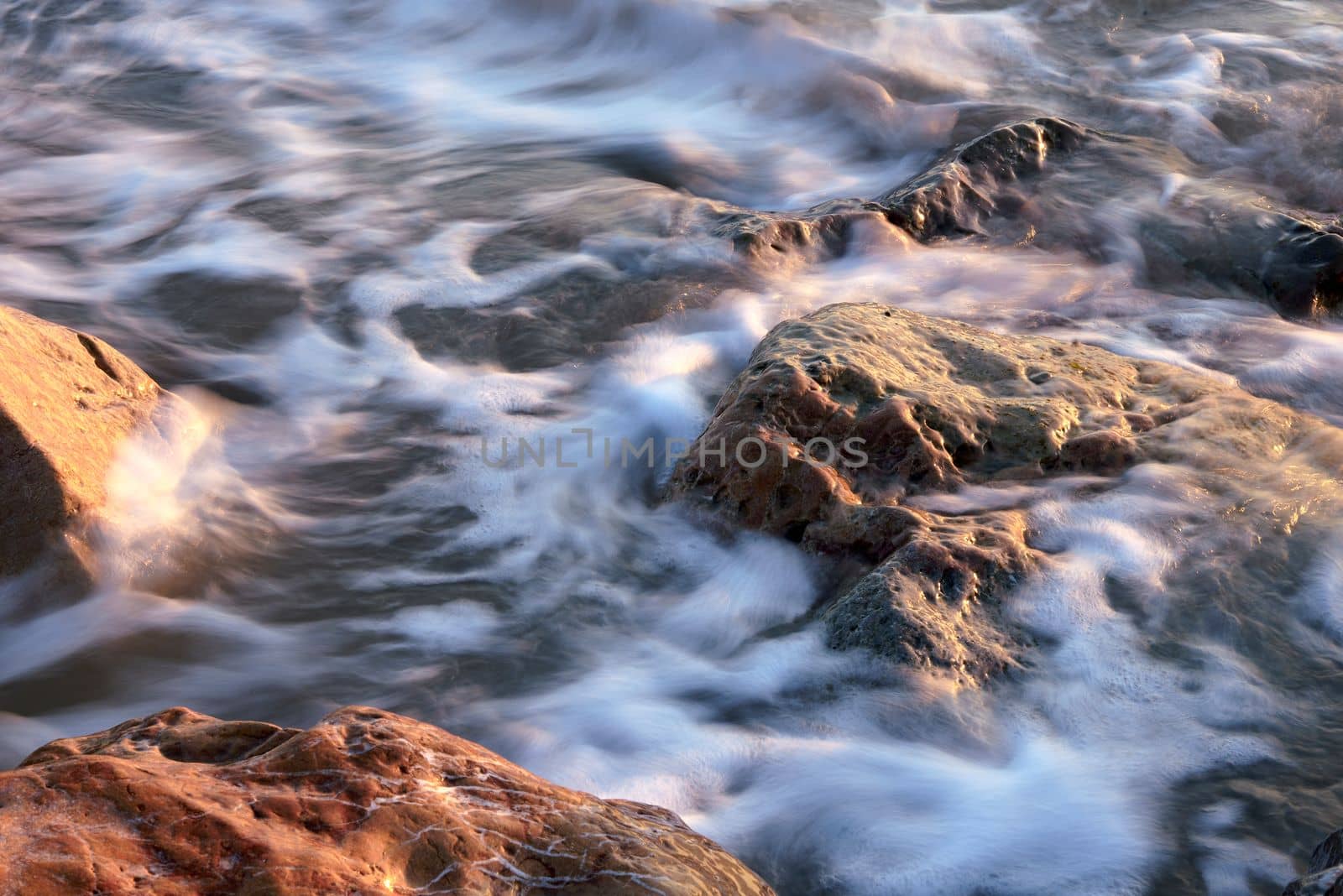 Line of stones from the coast at sunrise. Long exposure, silk effect water, big and small stones, sun rays, empty beach