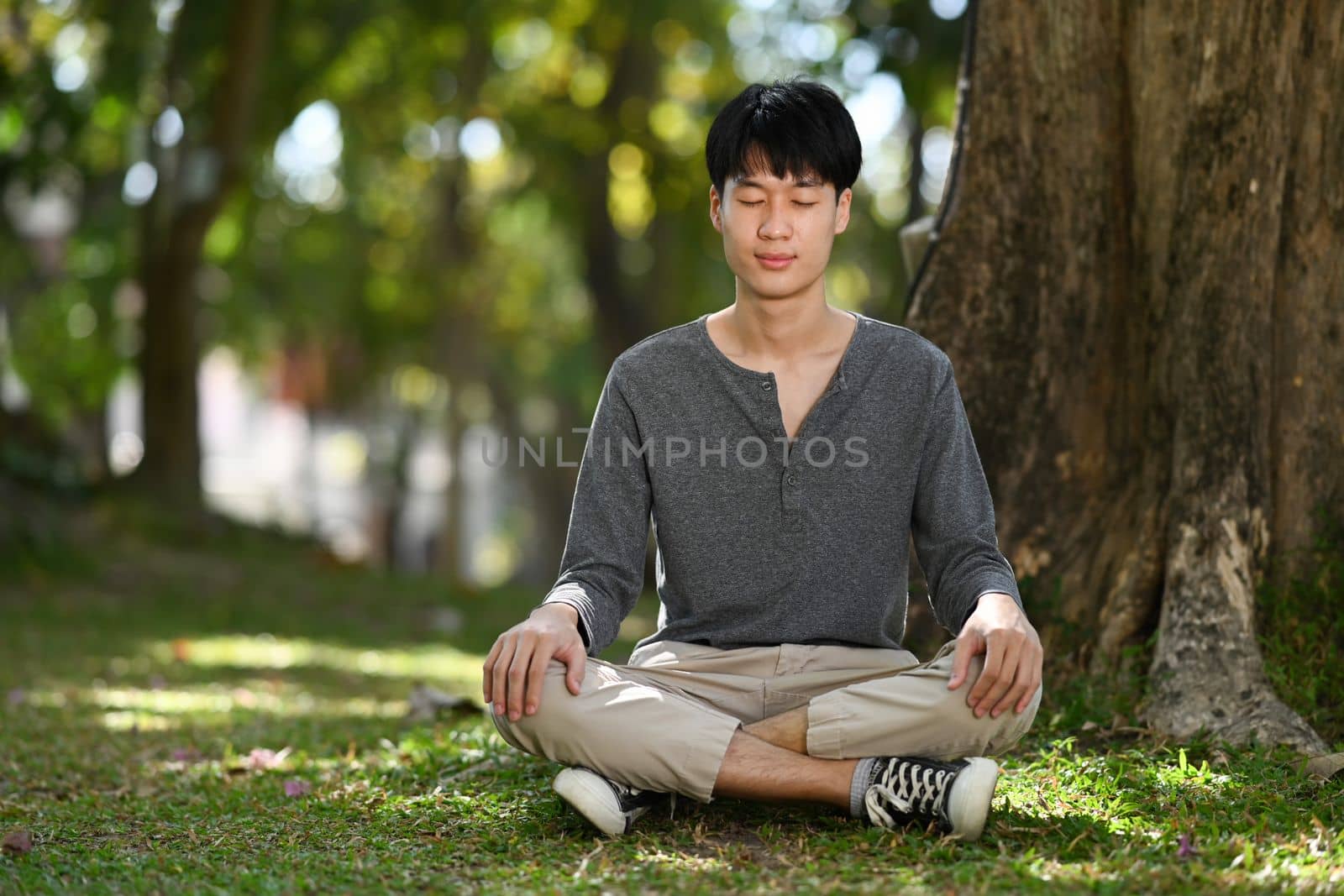 Pleasant asian man sitting in lotus pose sitting on green grass. Meditation and mental health concept by prathanchorruangsak