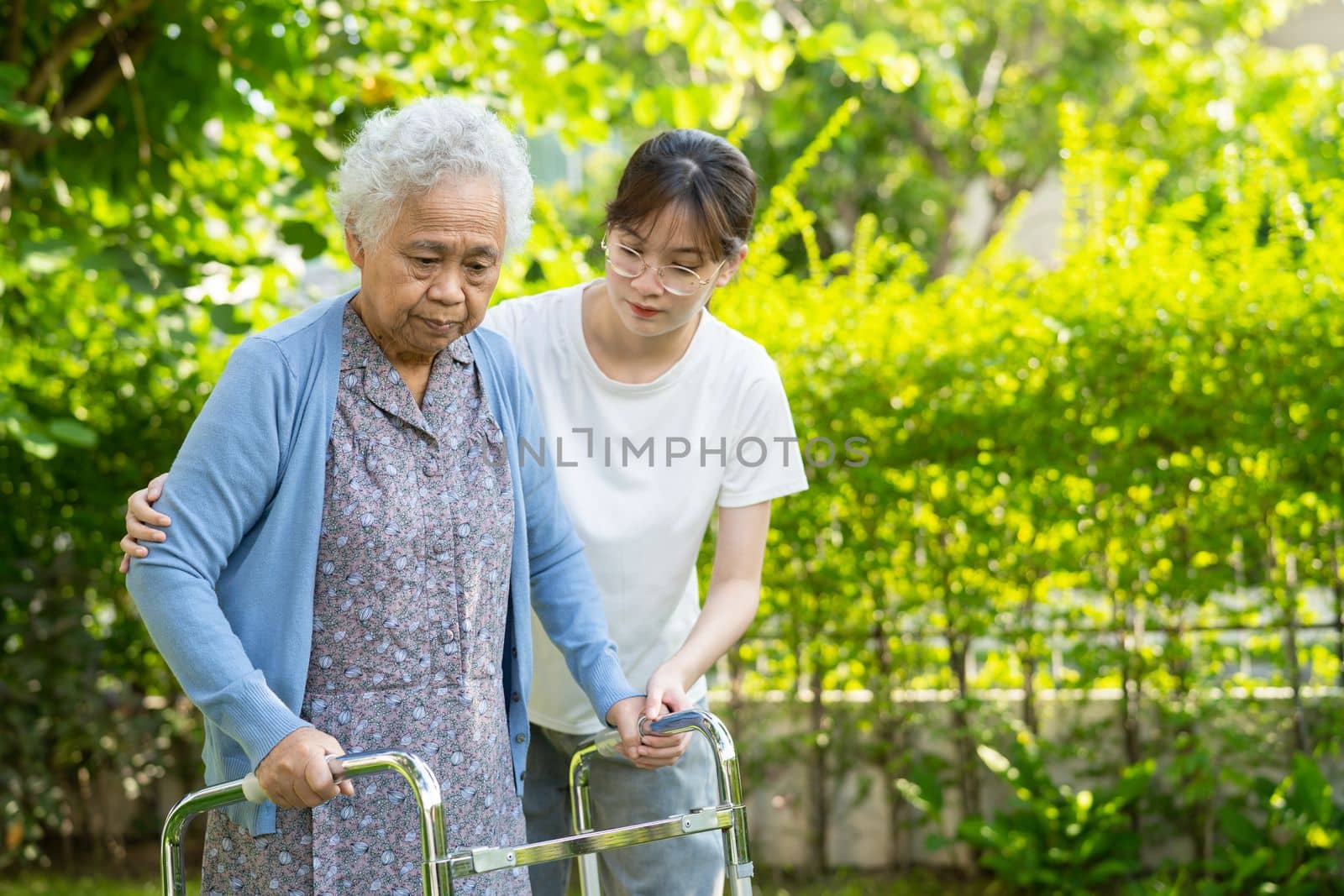 Caregiver help and care Asian senior or elderly old lady woman use walker with strong health while walking at park in happy fresh holiday.