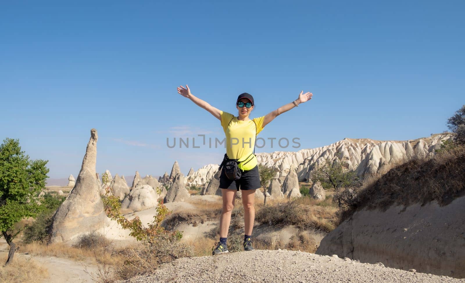 Woman tourist standing with raised hands on turkish mountains background in Cappadocia