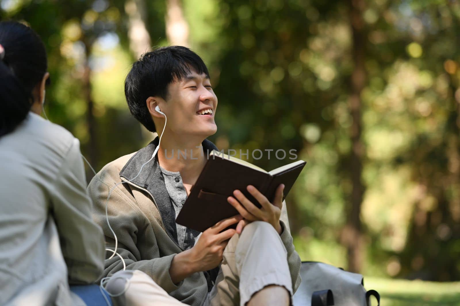 Lovely young couple sitting together in the park and listening to music with earphones.