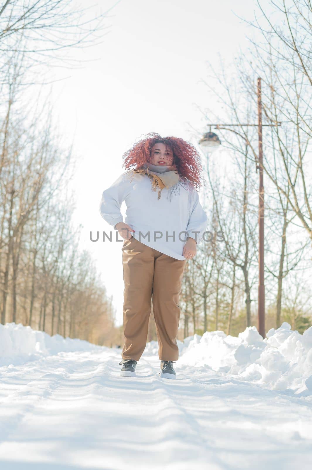 Smiling plump redhead woman jumping in park in winter. by mrwed54