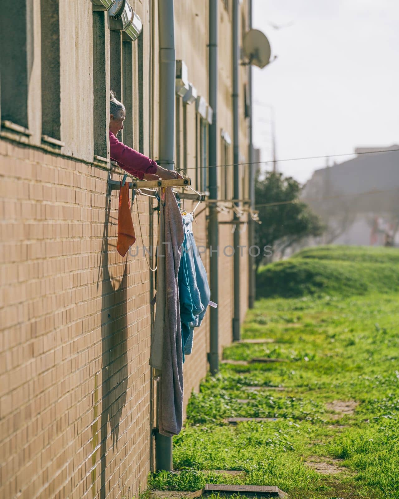 Old woman tends laundry hanging in the Portuguese sunshine in Espinho, Portugal. January 2023 by papatonic