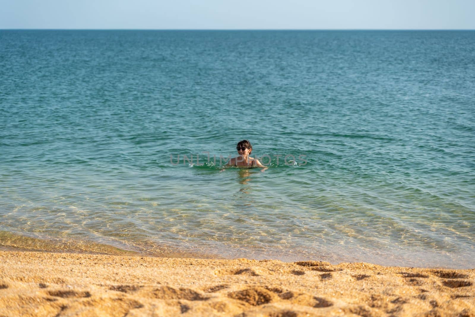 Woman sea swimsuit sand. The girl swims in the sea in a black swimsuit, the water is clean and transparent. Alone on the beach on a sunny day. by Matiunina