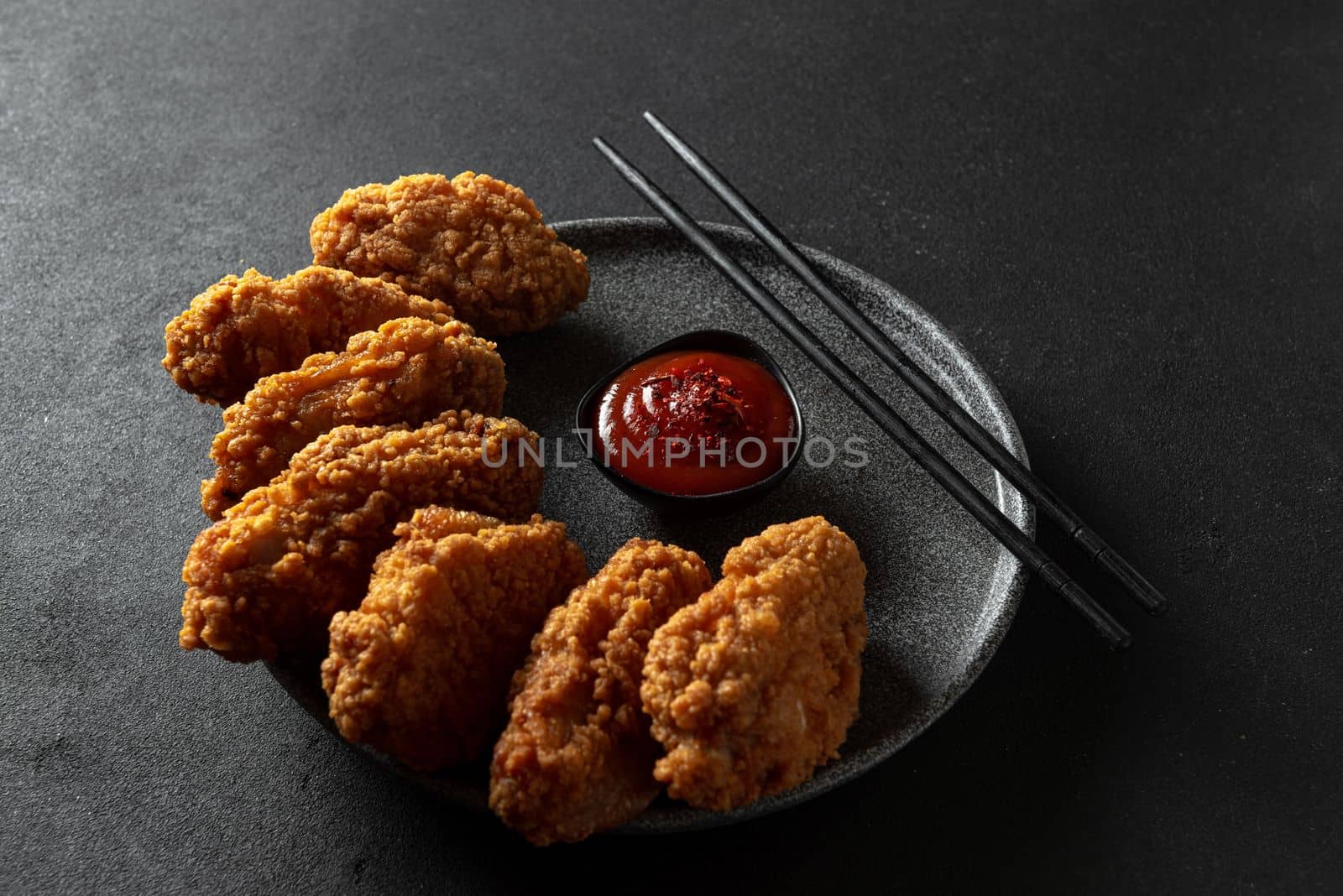 Spicy pieces of chicken fillet in crispy breading, on a black plate on a dark background, stone or concrete. Top view with a copying spot