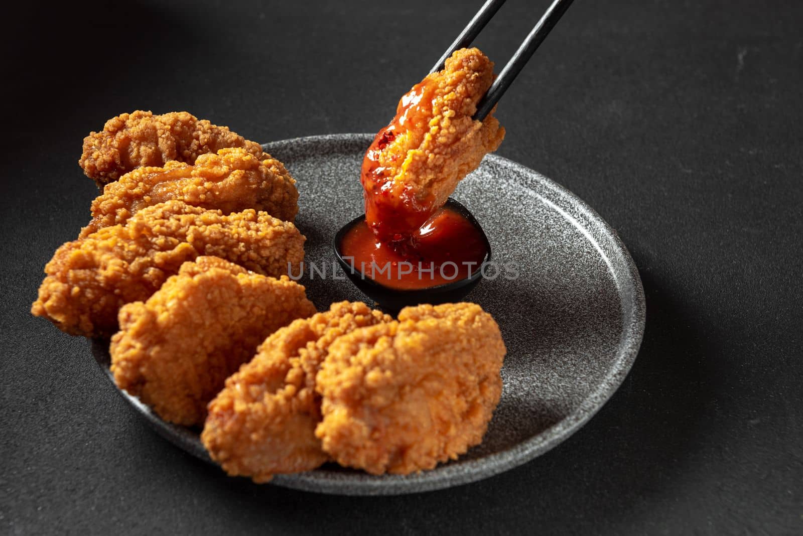 Spicy pieces of chicken fillet in crispy breading, on a black plate on a dark background, stone or concrete. Top view with a copying spot. by gulyaevstudio