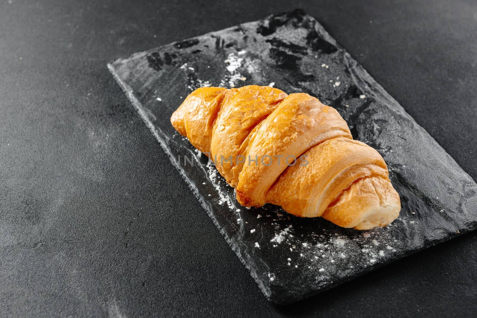 Large croissant on black background. Fresh and delicious French pastries, bakery concept, close-up image. Place to copy.