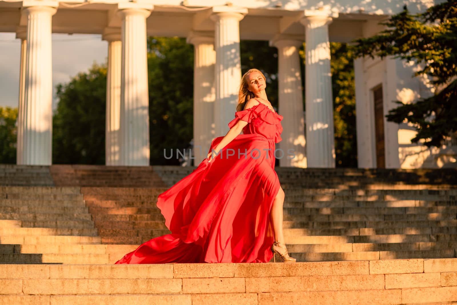 A woman in a long red dress against the backdrop of sunrise, bright golden light of the sun's rays. The concept of femininity, harmony