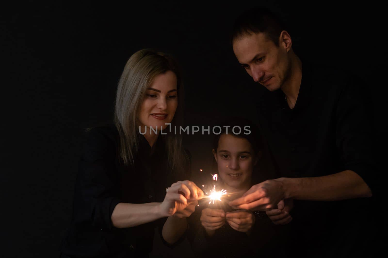 Young family with sparklers at Christmas time on a black background by Andelov13