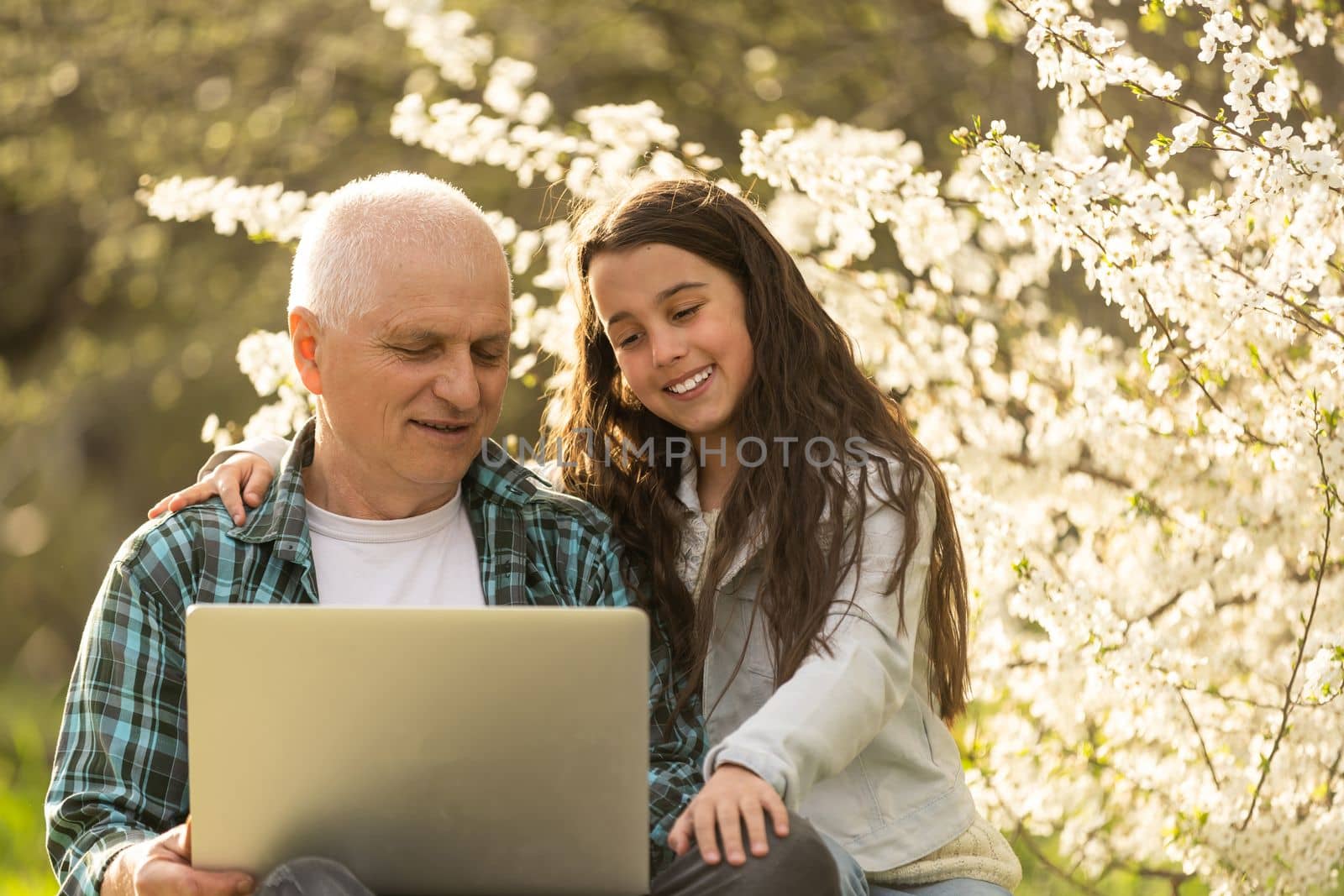 grandfather and granddaughter with laptop in the garden.