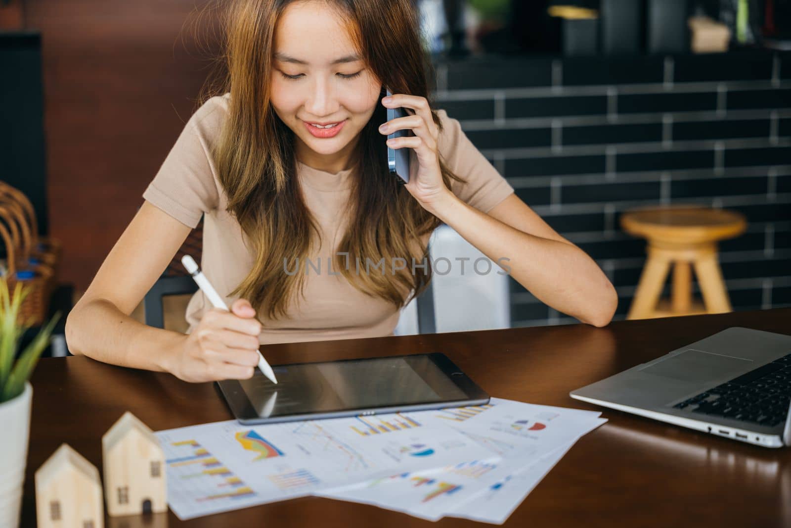 Asian businesswoman sitting at cafe calling mobile phone talking with customer asking about something, smiling female working laptop computer and writing take note on digital tablet at home office