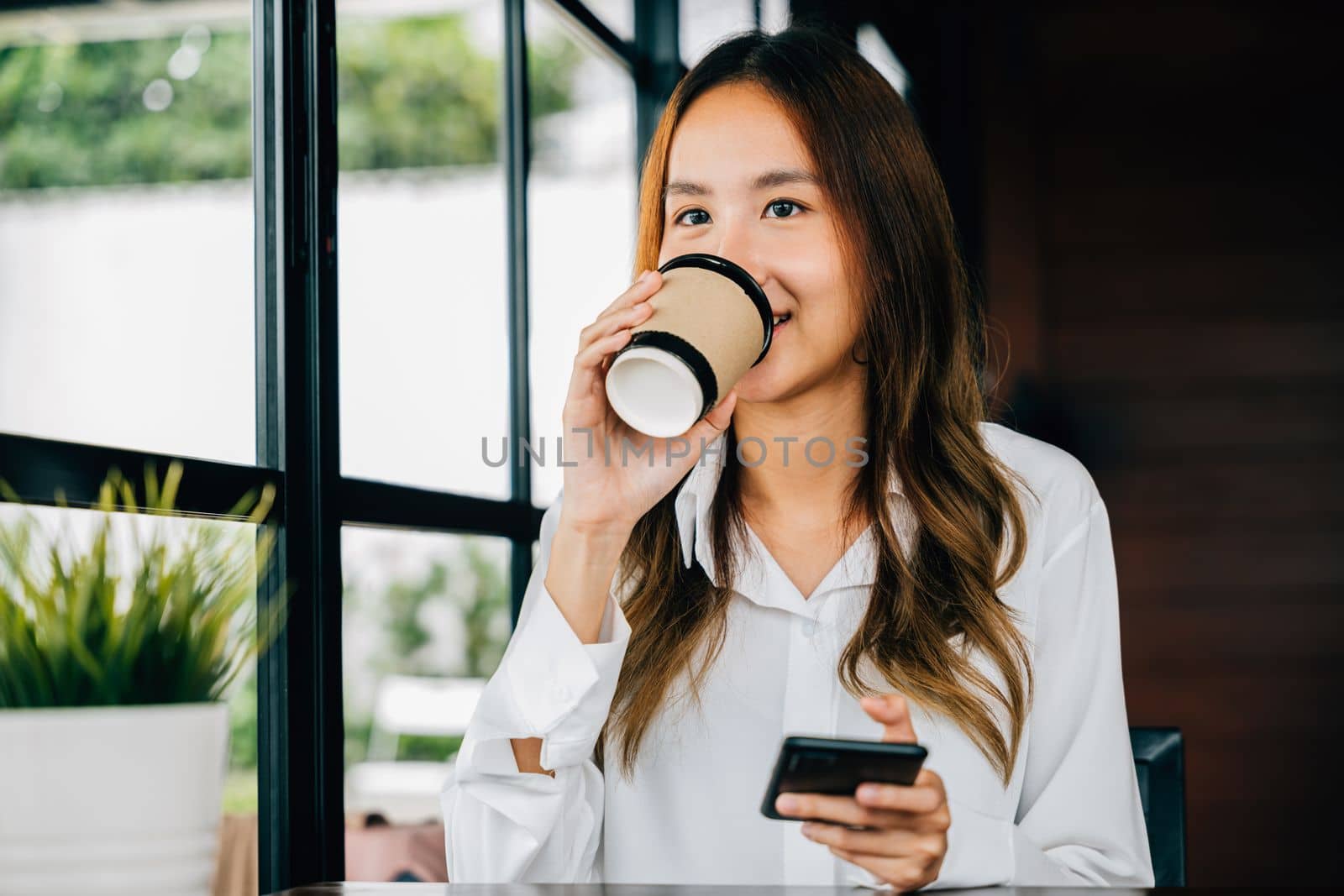 business woman holding coffee paper cup and using mobile phone to online chating at coffee shop by Sorapop