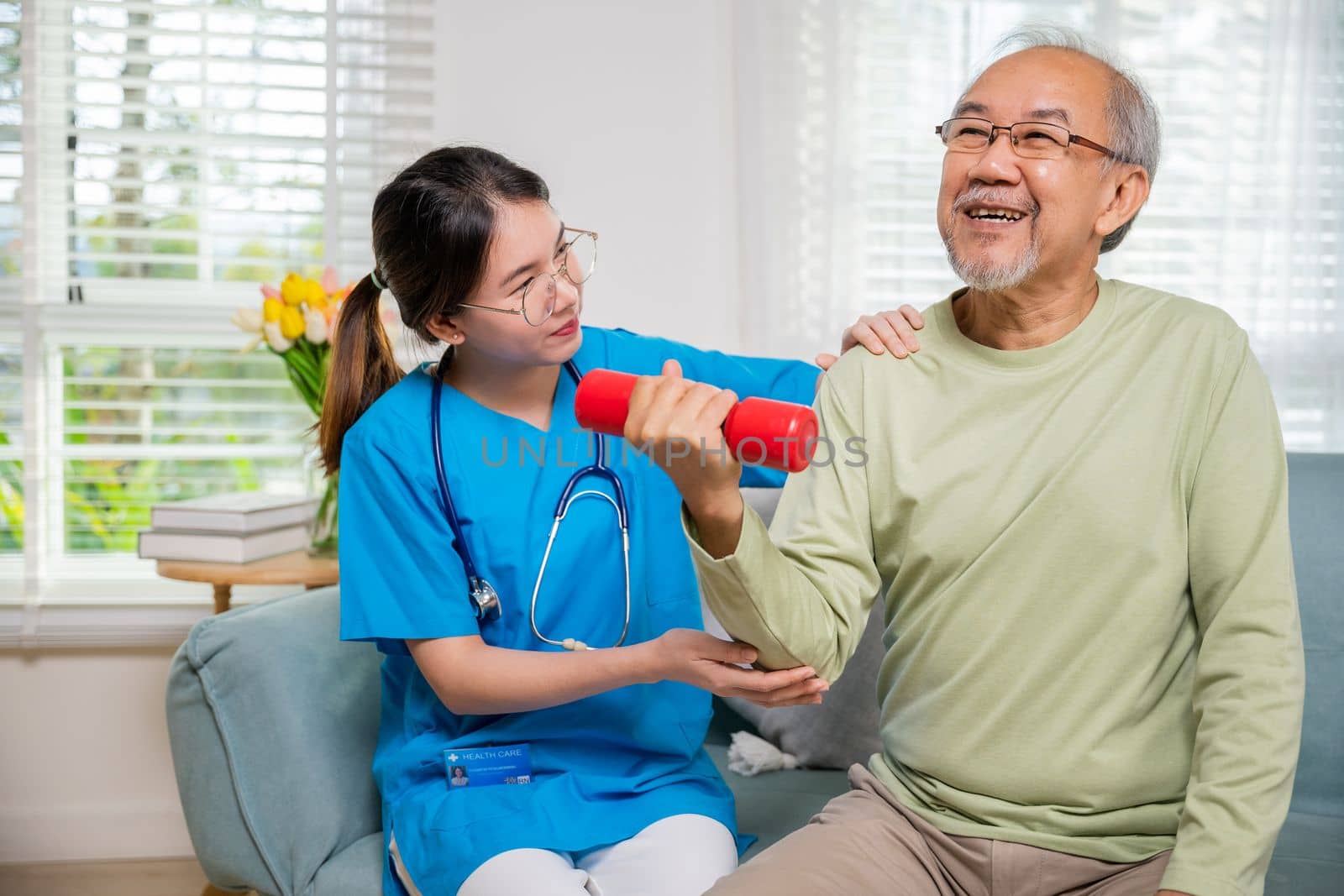 Asian nurse physiotherapist helping senior man in lifting dumbell at retirement home by Sorapop