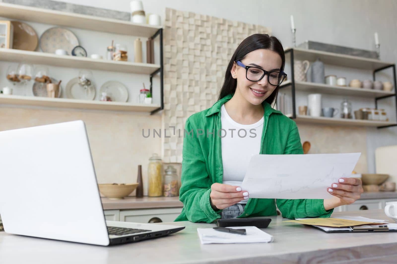 Young smiling woman designer works from home online. Holds documents, plans, drawings in his hands by voronaman