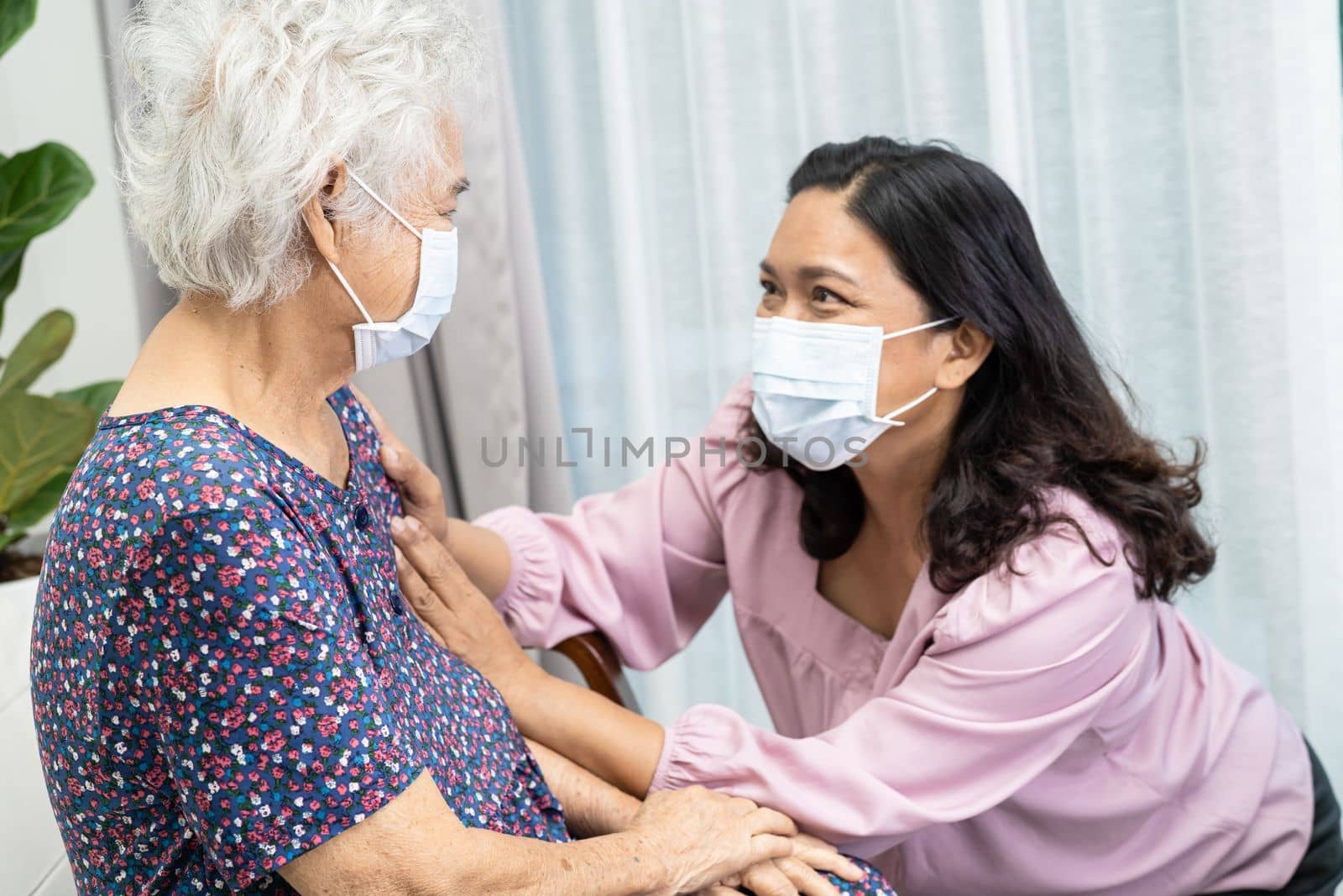 Caregiver help and talk with Asian senior or elderly old lady woman wearing a face mask for protect safety infection Covid19 Coronavirus in park. by pamai