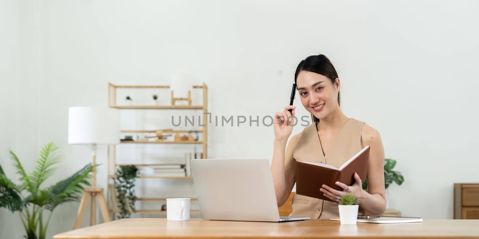 Happy Asian woman using laptop while taking note at home