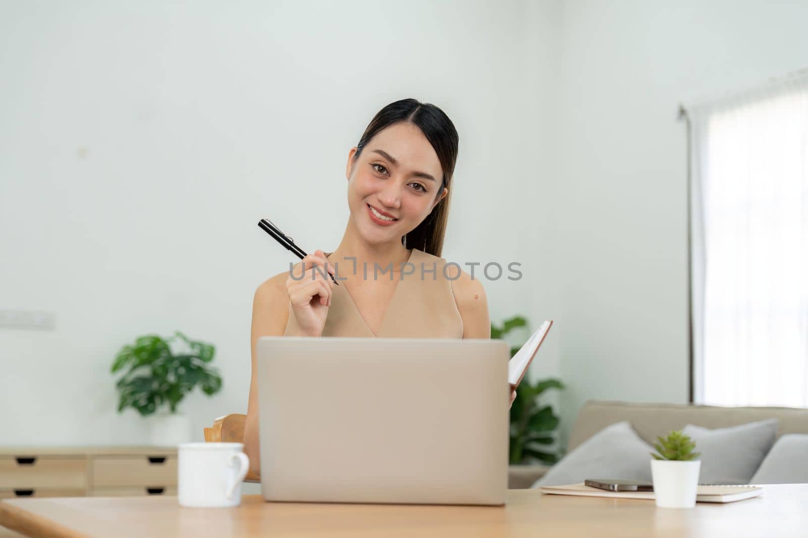 Young asian woman taking down notes in diary. Female university student preparing note for the exam at home office, online education and work from home concept by nateemee
