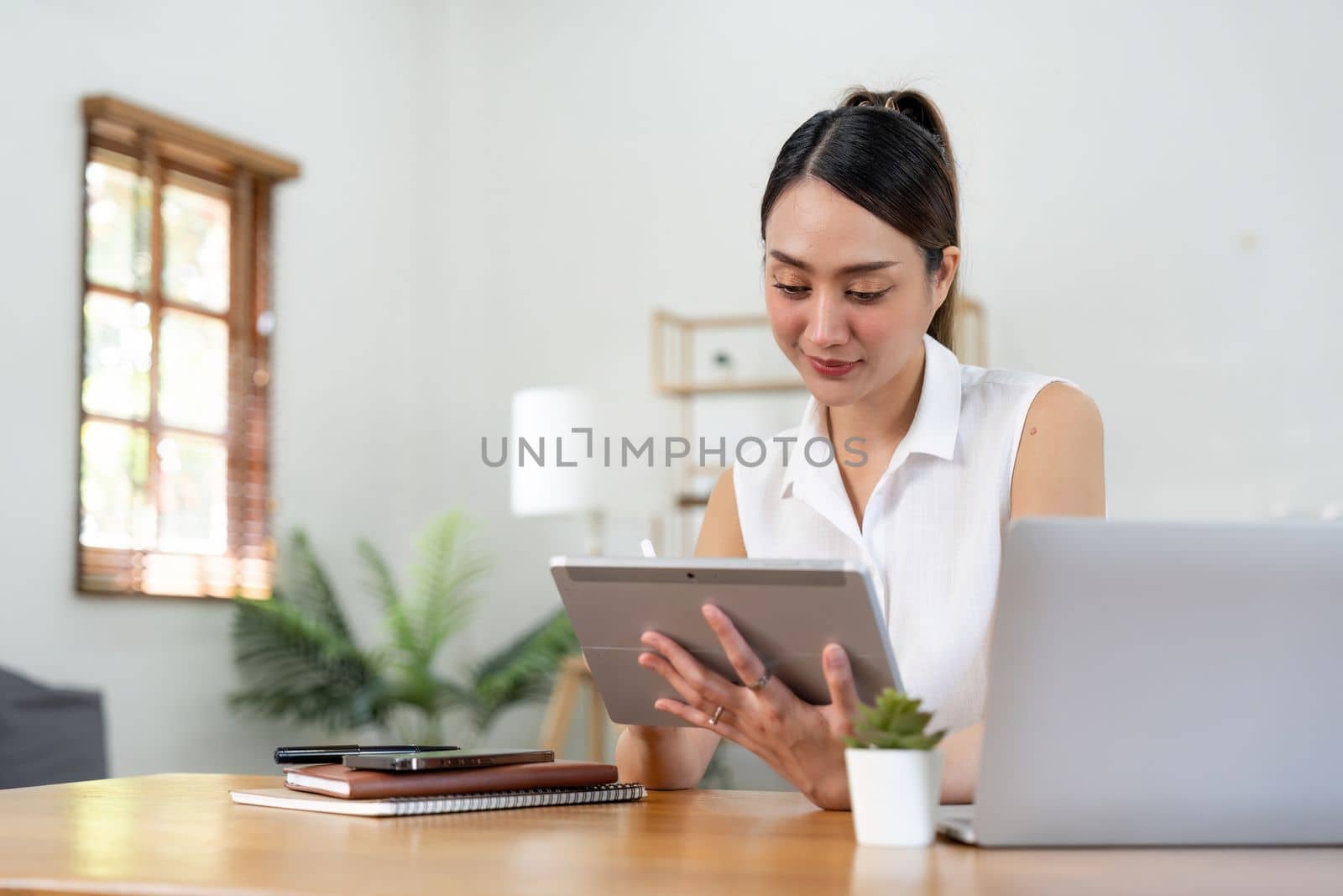 Portrait of young asian woman holding stylus pen while working on tablet computer at home.