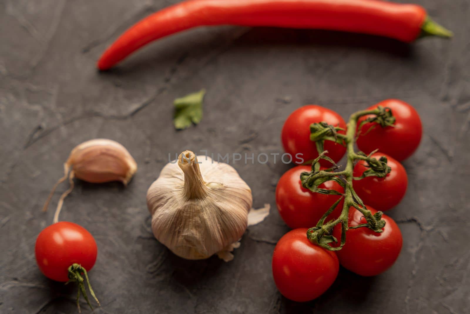 Delicious ripe cherry tomatoes, chili peppers and garlic for cooking on a dark background. Top view.