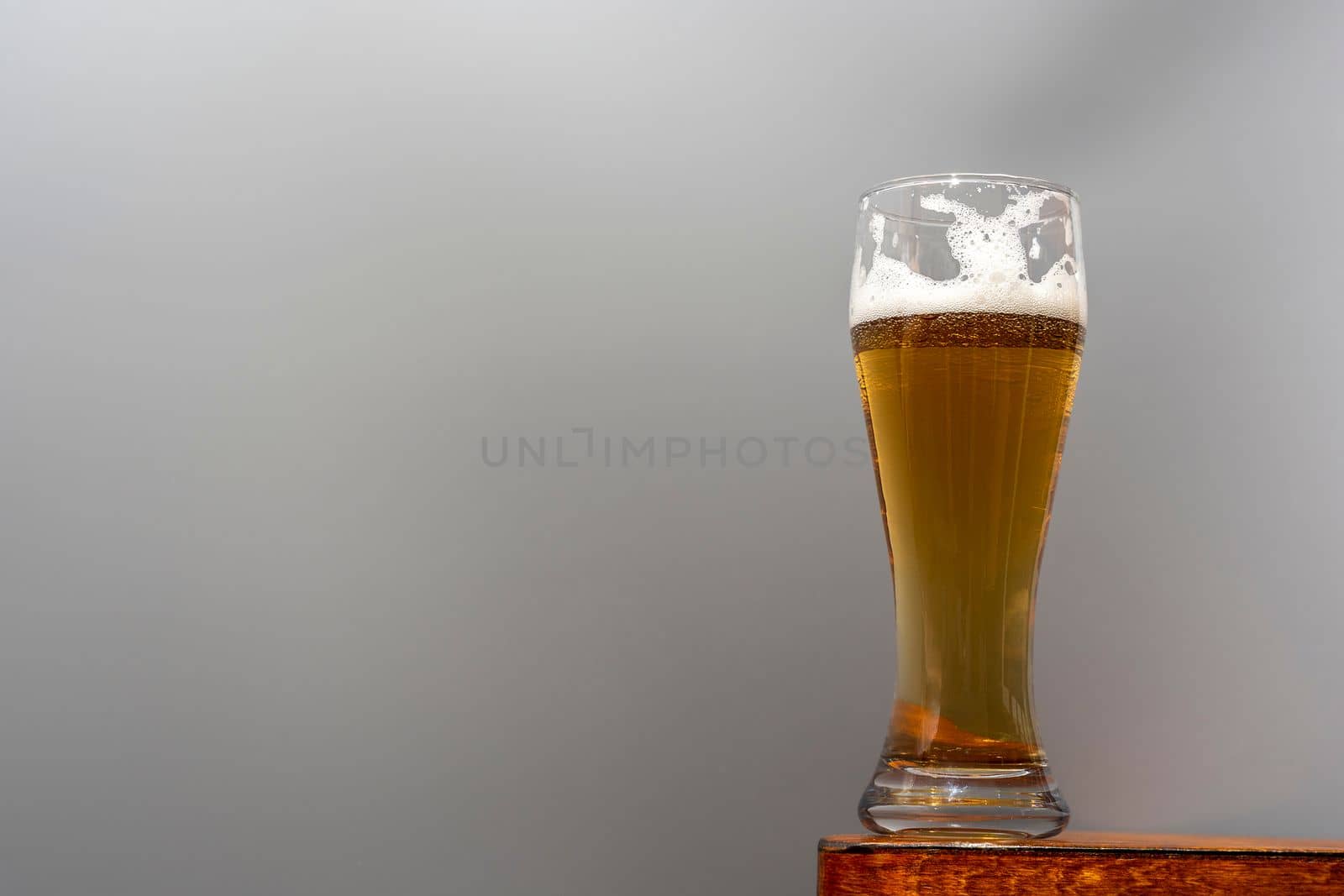 A glass of fresh and cold beer on a wooden table on a grey background. A glass of light craft beer.