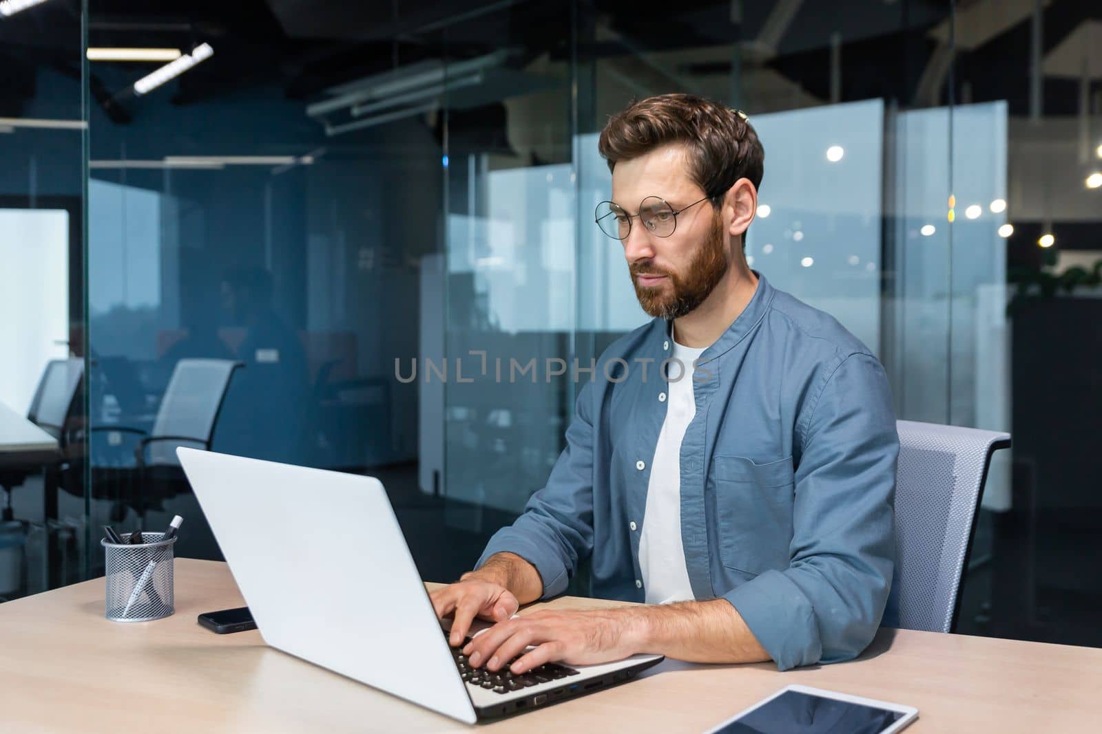 Serious young man freelancer, designer, IT specialist works concentratedly in the office, co-working space. Sitting at a table with a laptop.