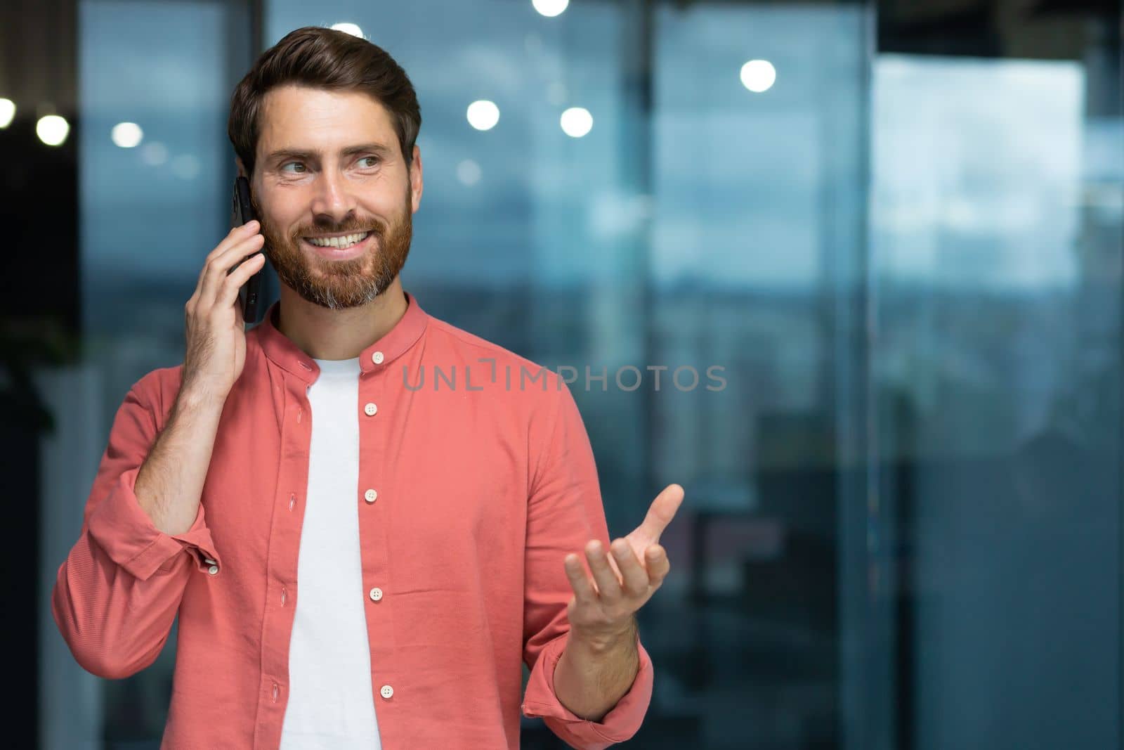Portrait of a young handsome man standing and talking on the phone indoors, office.