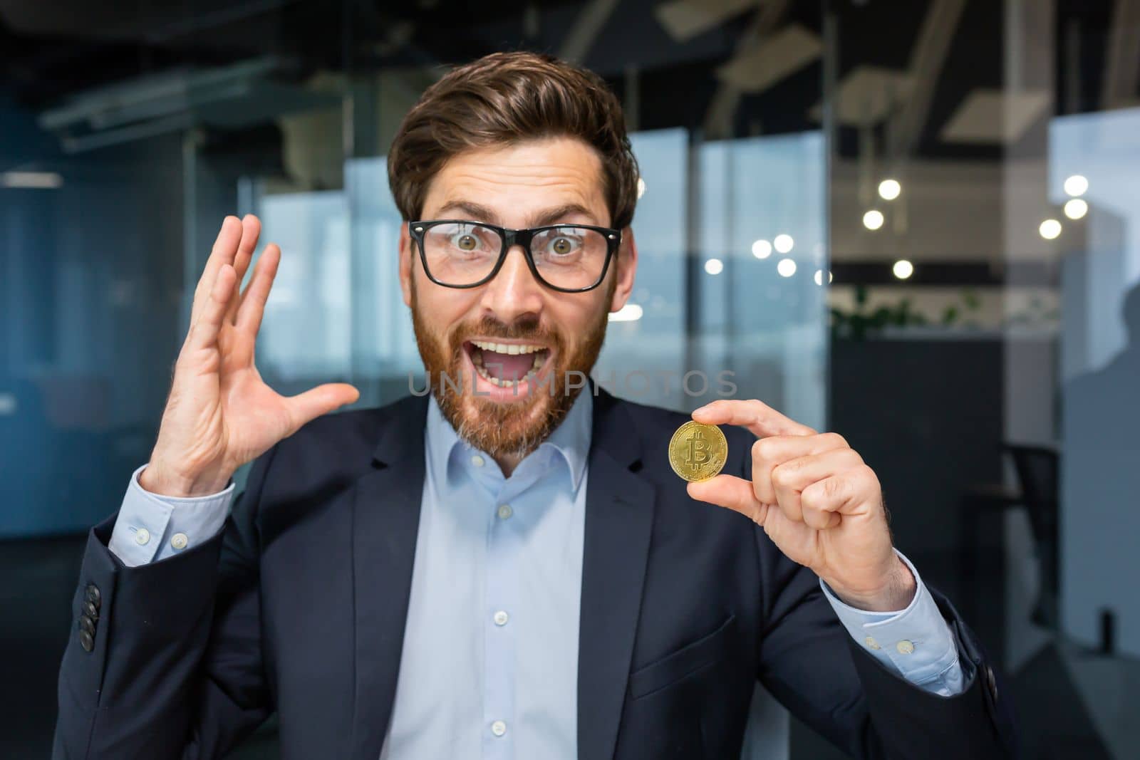 Concept, close-up photo. A young business man holds a gold coin, cryptocurrency in his hand. He looks at the camera, screams with happiness