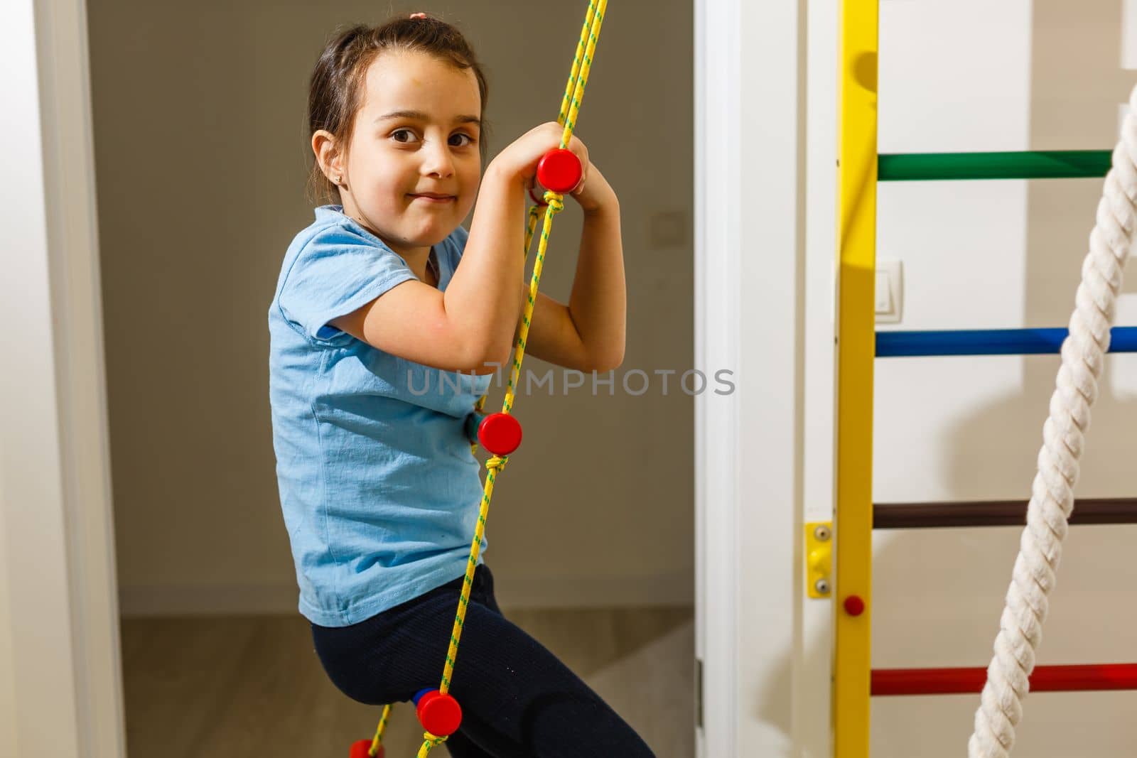 The girl smiles, plays and goes in for sports on the stairs and the Swedish wall in the children's center in special tight clothes and leads a healthy lifestyle under the supervision of her parents.