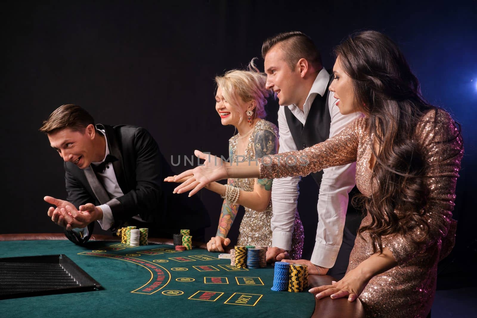 Side shot of a confused rich buddies playing poker at casino. Youth have lose. They are standing at the table against a red and blue backlights on black background. Risky gambling entertainment.