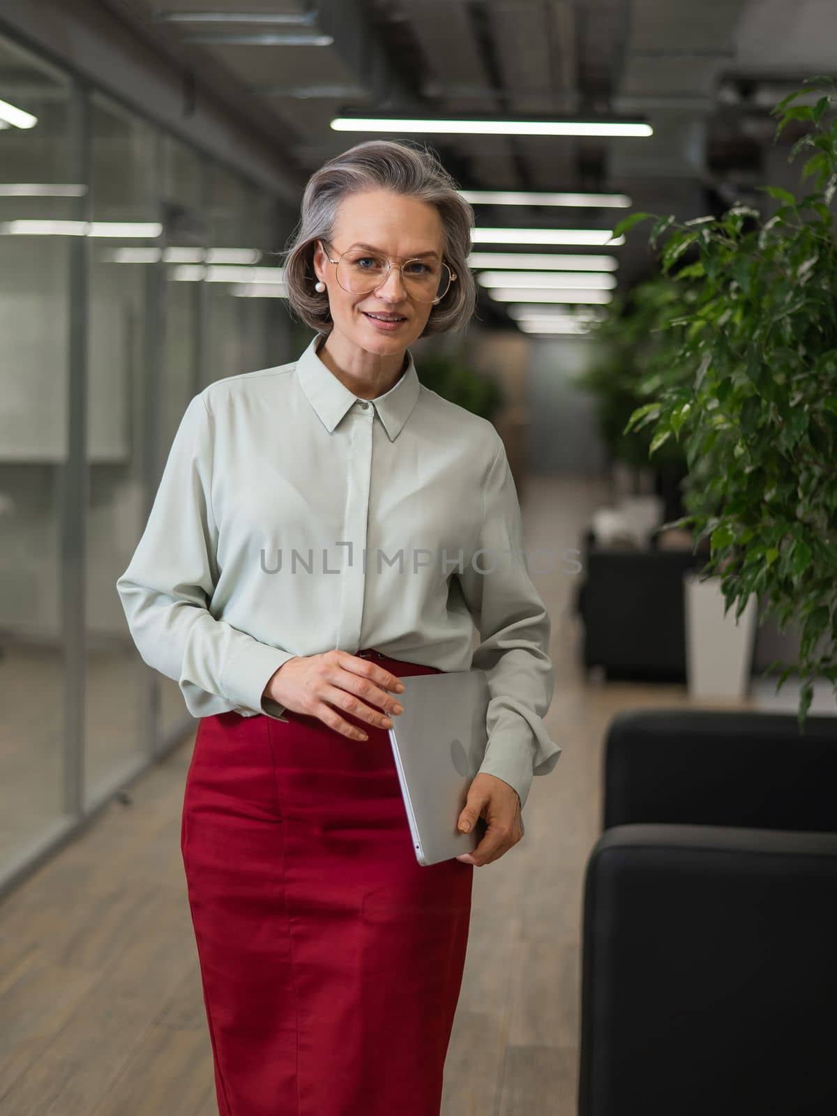 Attractive mature caucasian woman holding laptop while standing in office