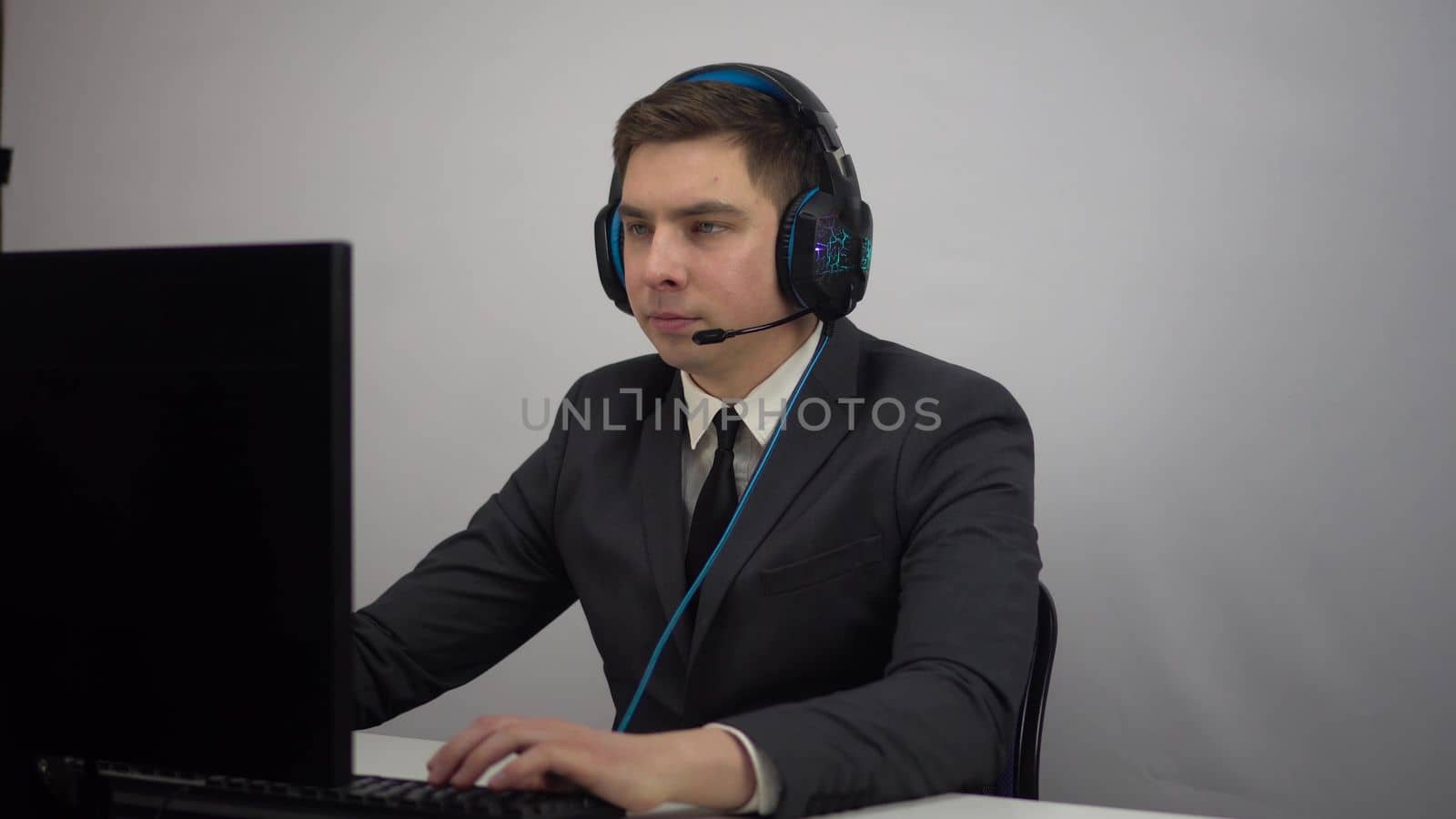 A businessman plays an online computer game while sitting in the office. A young man in a suit and headphones plays with a microphone. 4k